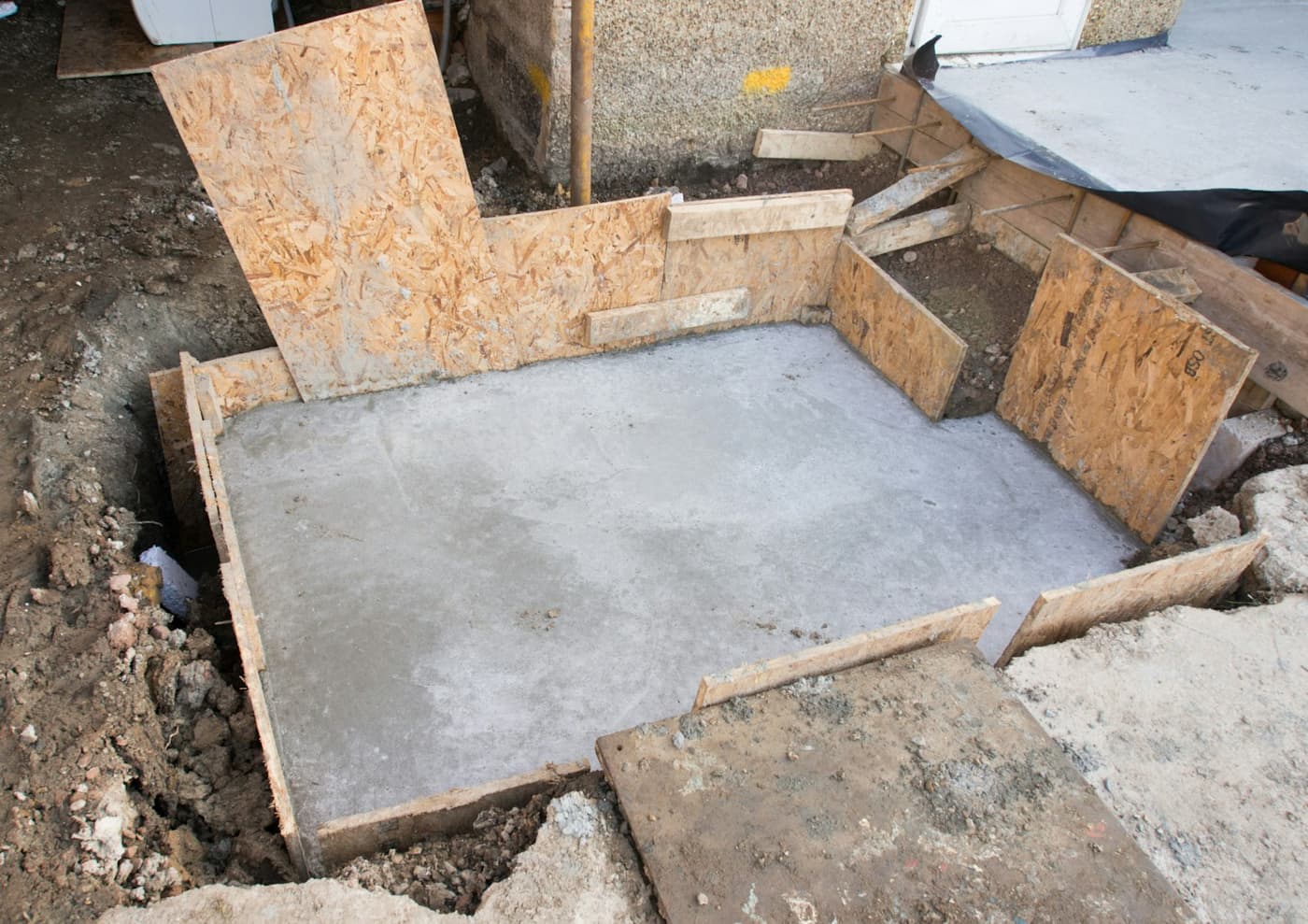 Fresh concrete poured in formwork against a house foundation wall
