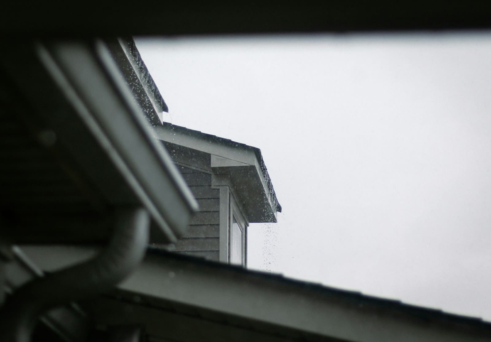 Rain dripping off the eaves and gutter of a house on a grey day